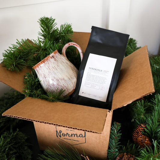Open cardboard box with a ceramic mug, coffee package, and Christmas decorations.